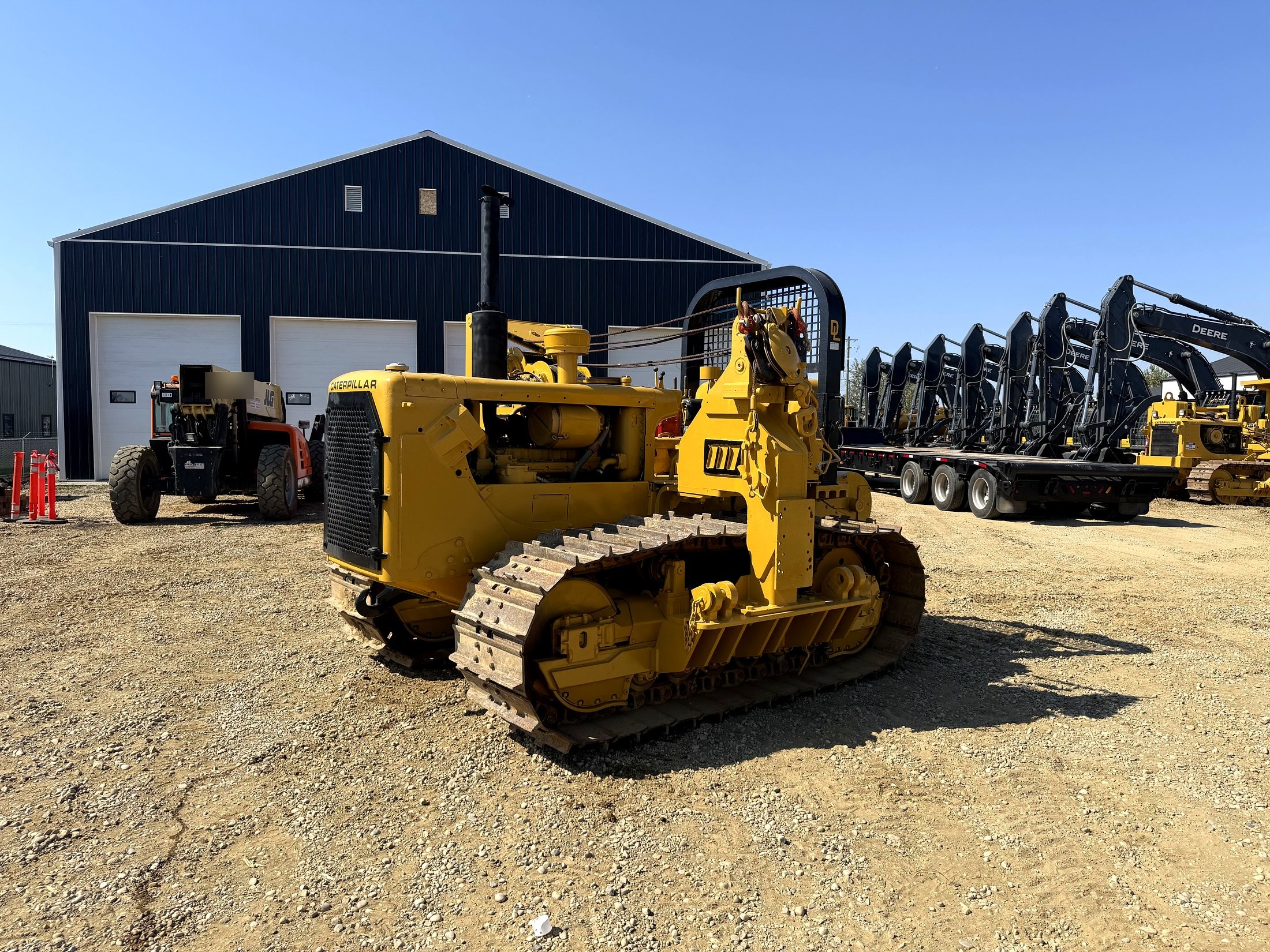 Caterpillar pipelayer dozer with a row of John Deere excavators staged behind it