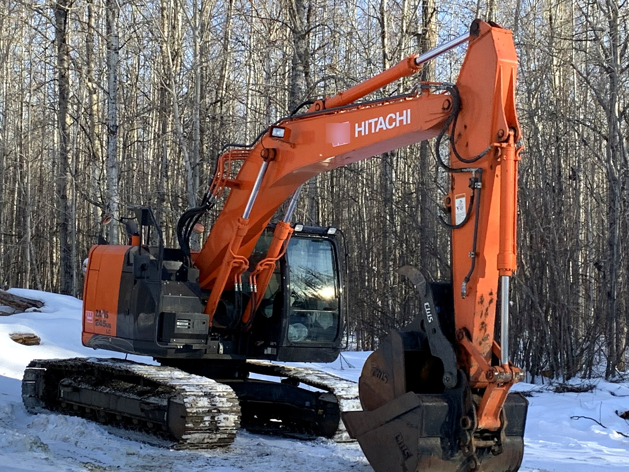 Hitachi ZAXIS 245US LC excavator, full machine, parked at the treeline on a snow-covered jobsite